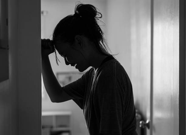 A black-and-white image of a distressed woman leaning against a wall with her head down, appearing upset. The image conveys emotions of sadness, frustration, or emotional struggle, symbolizing the pain of being disliked or hated by others without clear reasons. It reflects themes of rejection, misunderstanding, and emotional burden.
